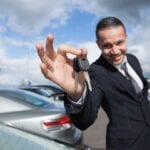 A man holding up his car keys in front of some cars.