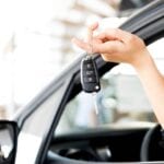 A person holding keys to their car in the drivers seat.