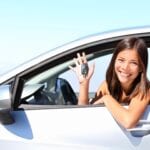 A woman sitting in her car holding up the keys.